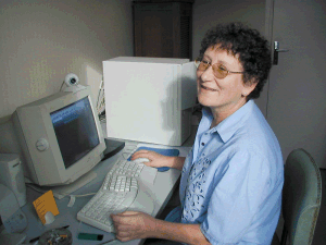 Martine sitting at her desk, smiling at the camera, in front of a beige CRT computer with a webcam perched on top